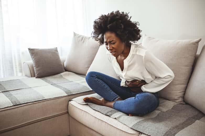 Black woman with period and pelvic pain, holding her stomach.